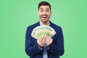 Young man with surprised smile as he is holding fan of euro notes in cash that he is lottery winner, feeling excited and happy, isolated on green background